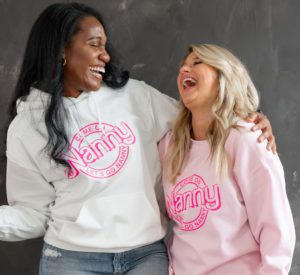 The Nanny League girl Barbie-themed sweatshirt on two models. One is light pink and one is white, both with hot pink "Come on Nanny Let's go Nanny"