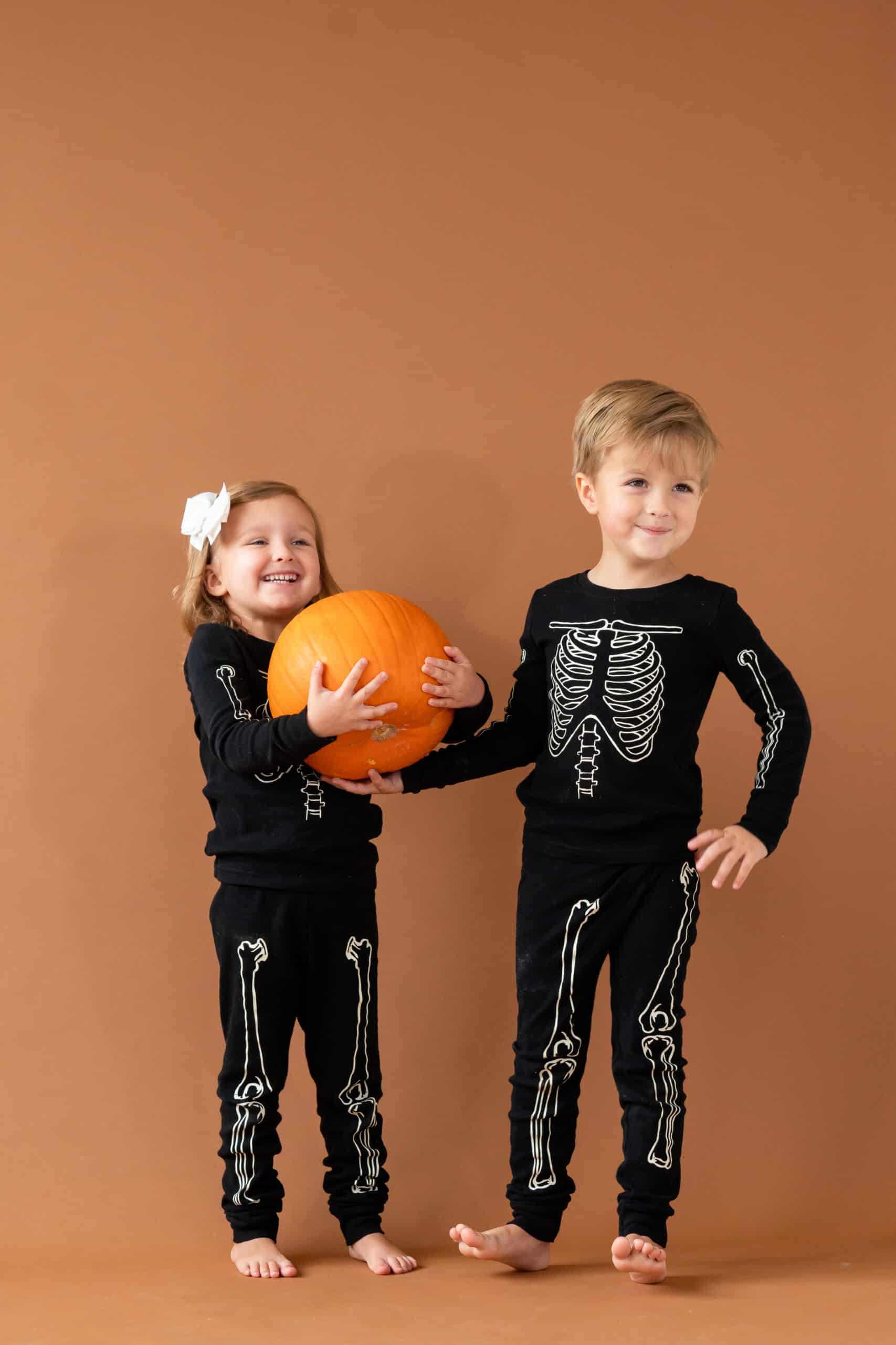 Brother and sister in family-themed halloween costumes holding a pumpkin.