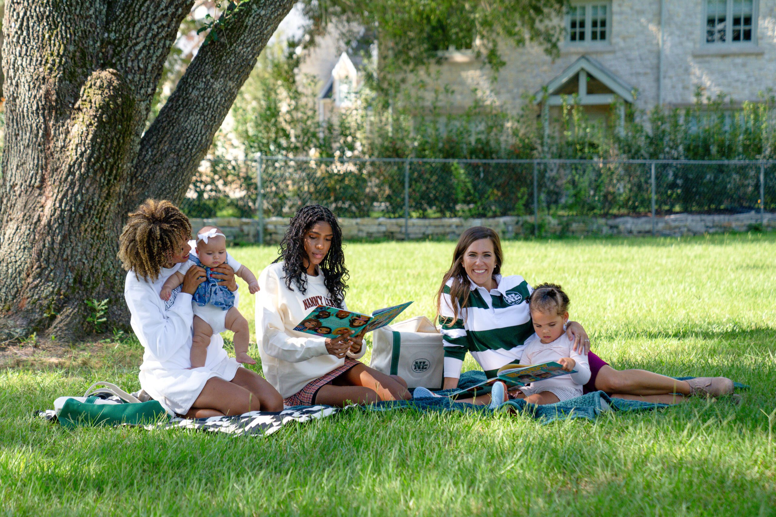 Nannies from The Nanny League with their nanny kids outside. Two nannies are reading to the children and the other nanny is playing with their nanny kid